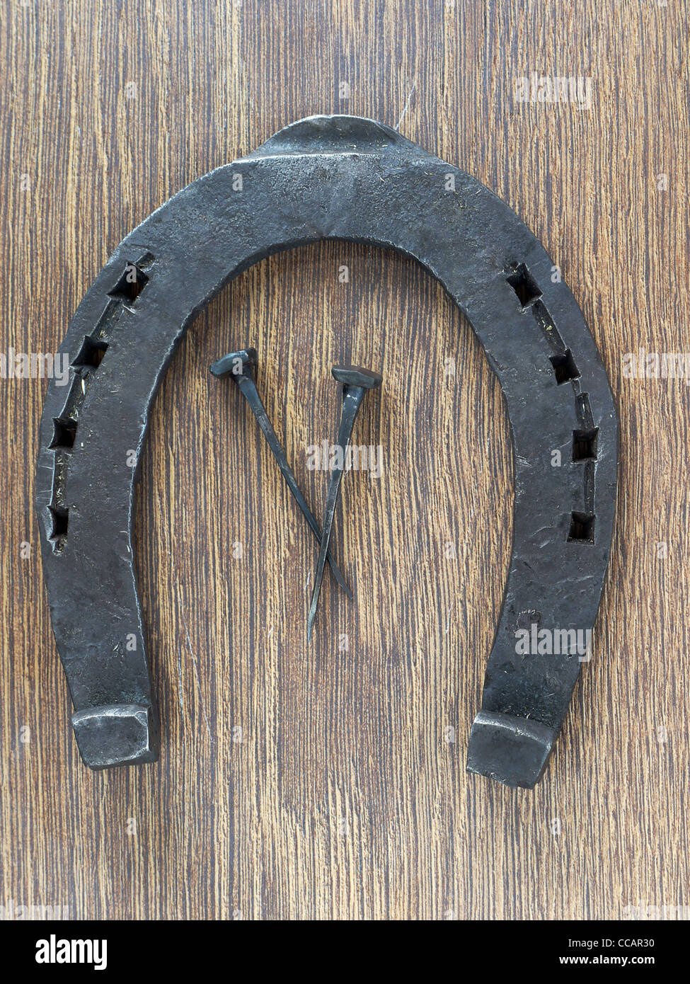 Horseshoe and two horseshoe nails on wooden plank Stock Photo