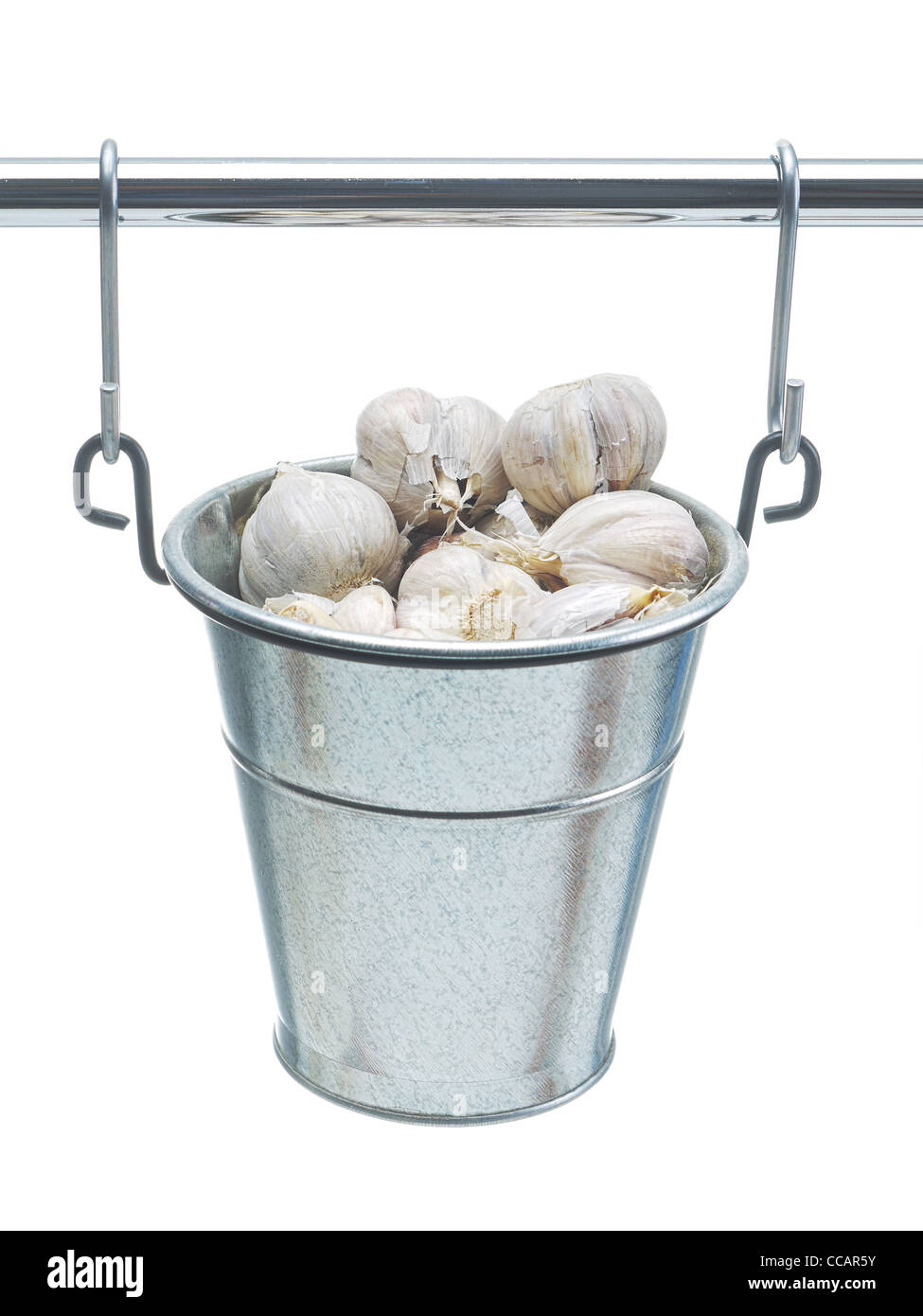 Cloves of garlic in small metal bucket hanging on railing over white background Stock Photo