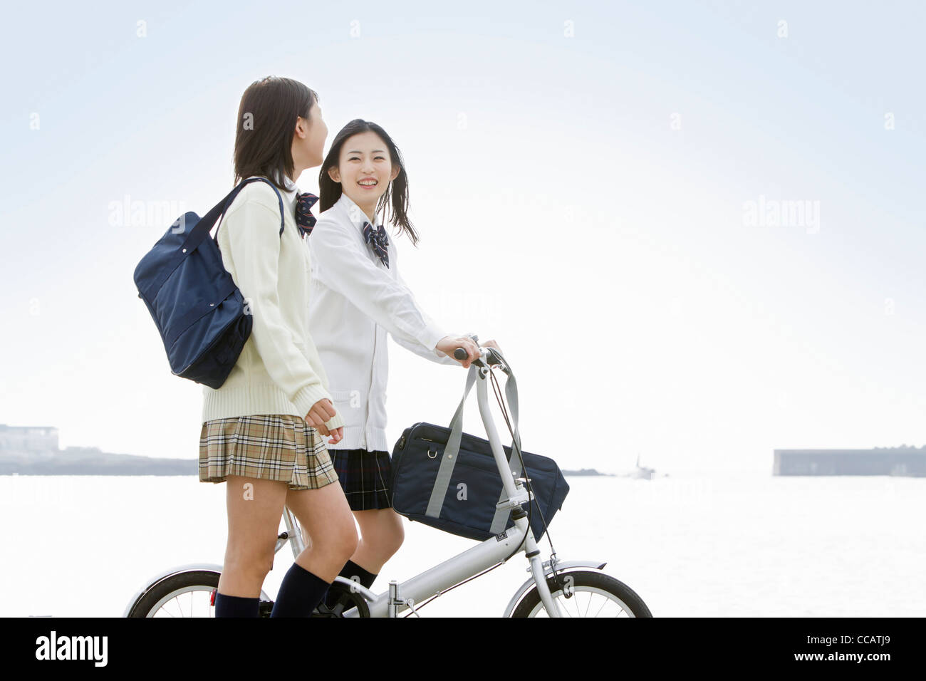 Two high school girls walking with a bicycle Stock Photo