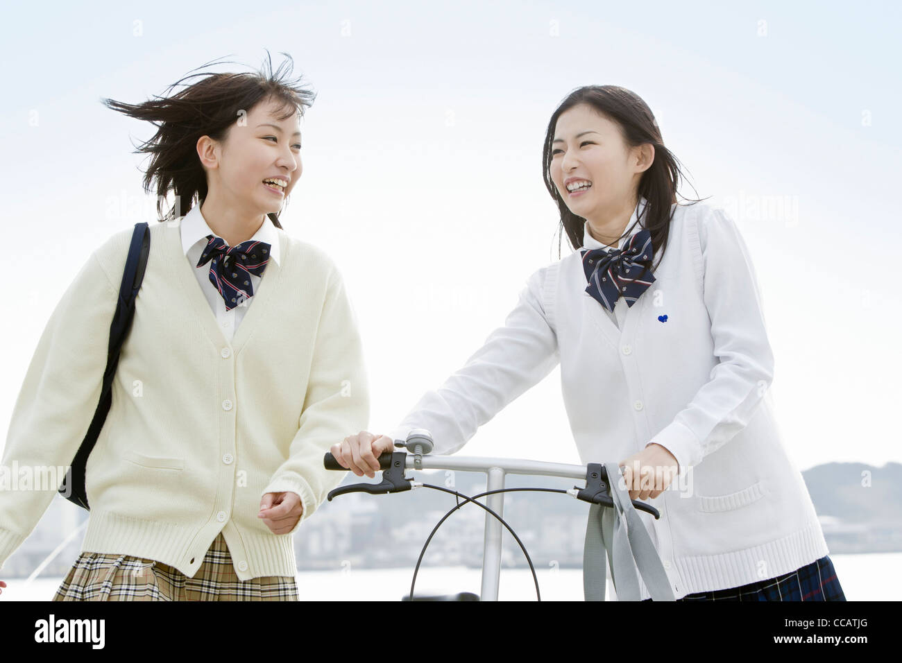 Two high school girls walking with a bicycle Stock Photo