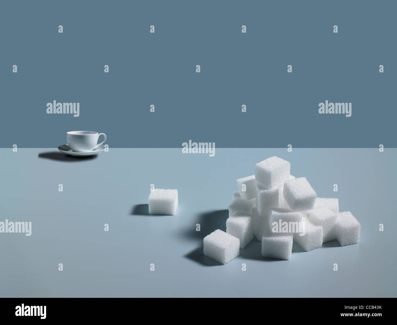 A pile of sugar cubes with a cup in the background on a blue background Stock Photo