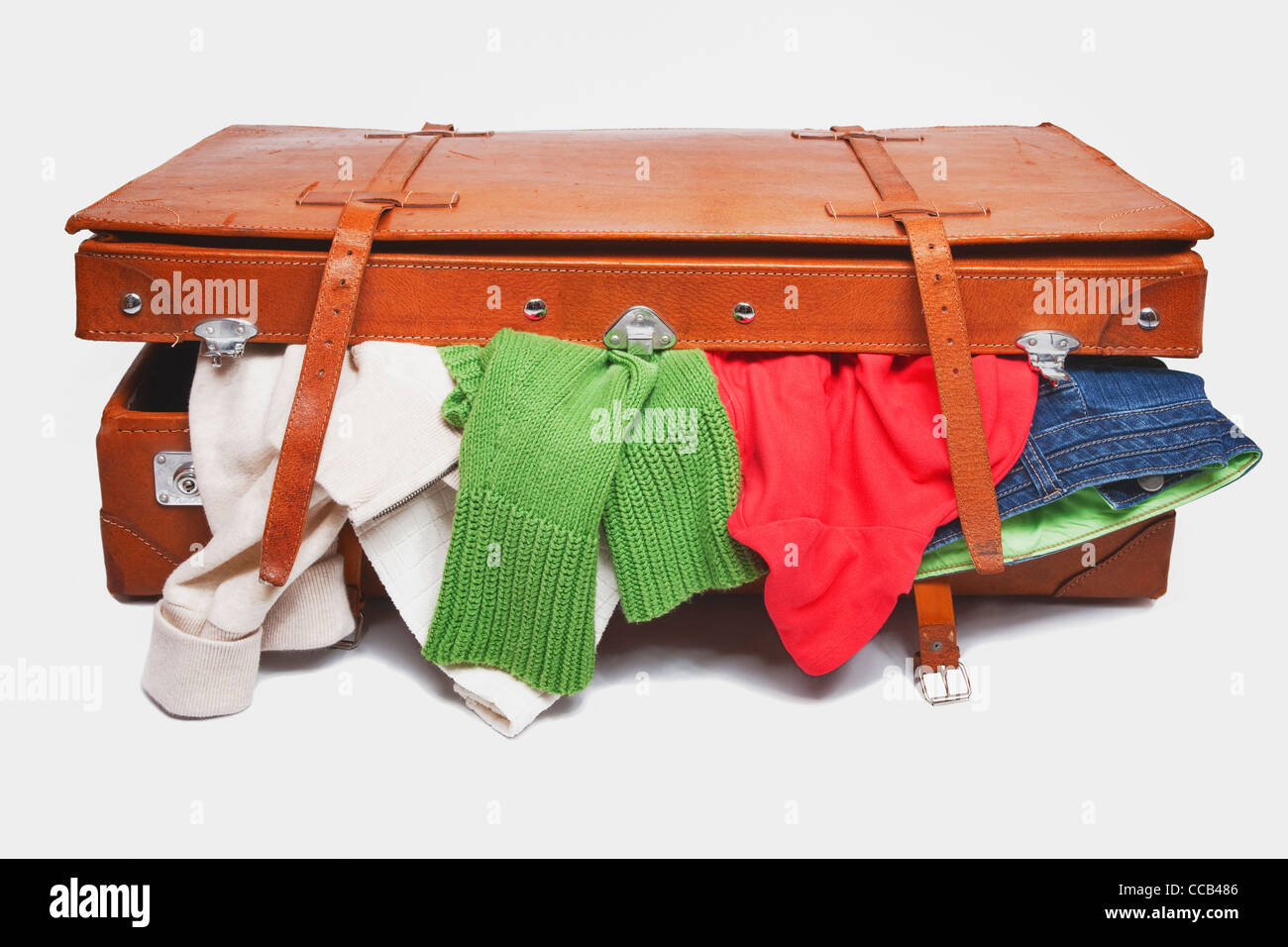 ein alter brauner Lederkoffer aus dem Kleidung herausquillt | clothes ooze out an old brown leather suitcase Stock Photo