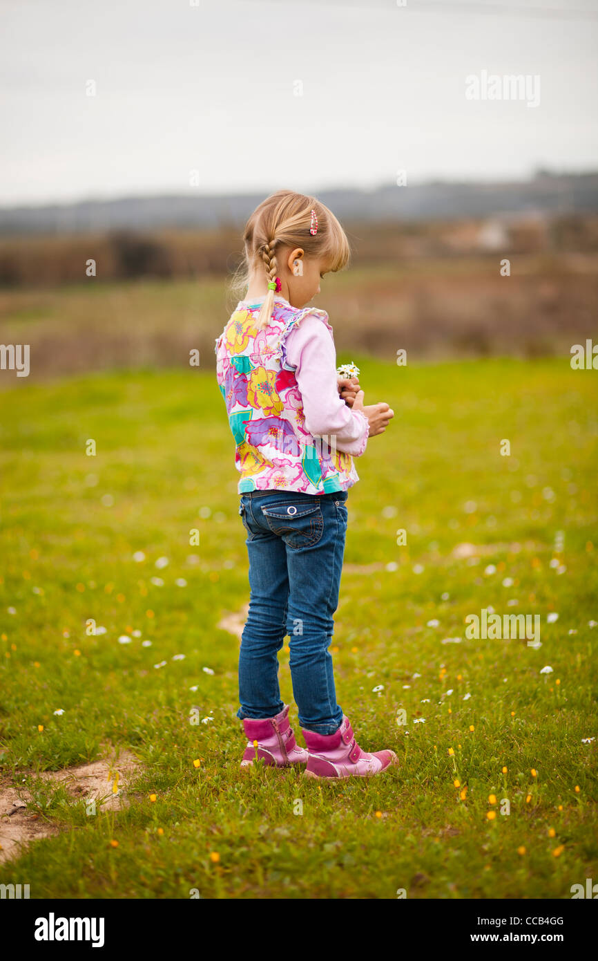 Cute little girl standing on a green field with flowers Stock Photo - Alamy