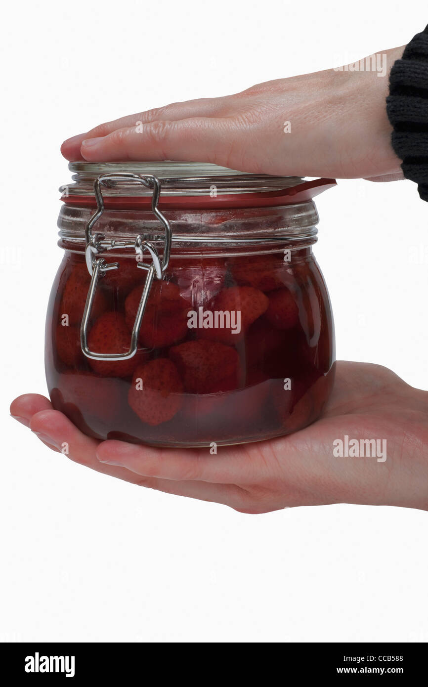 Ein Glas mit eingeweckten Erdbeeren wird in den Händen gehalten | a jar with home canned strawberries is hand-held Stock Photo