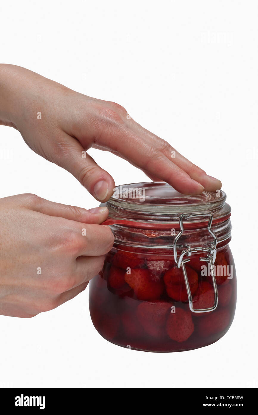 Ein Glas mit eingeweckten Erdbeeren wird geöffnet | a jar with home canned strawberries will be opening Stock Photo
