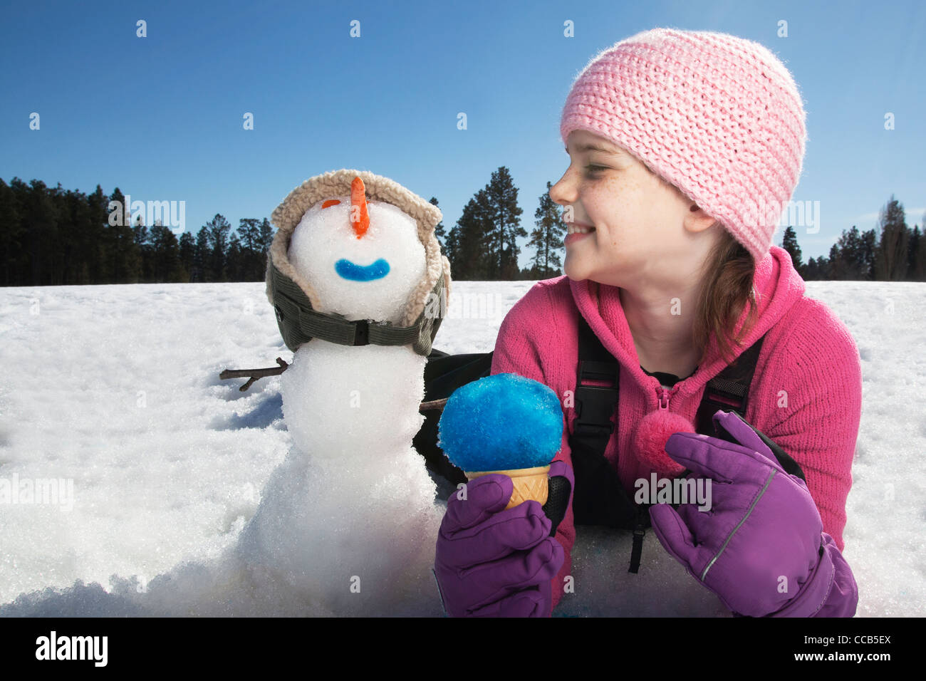 Girl laying in snow with snowman. Stock Photo