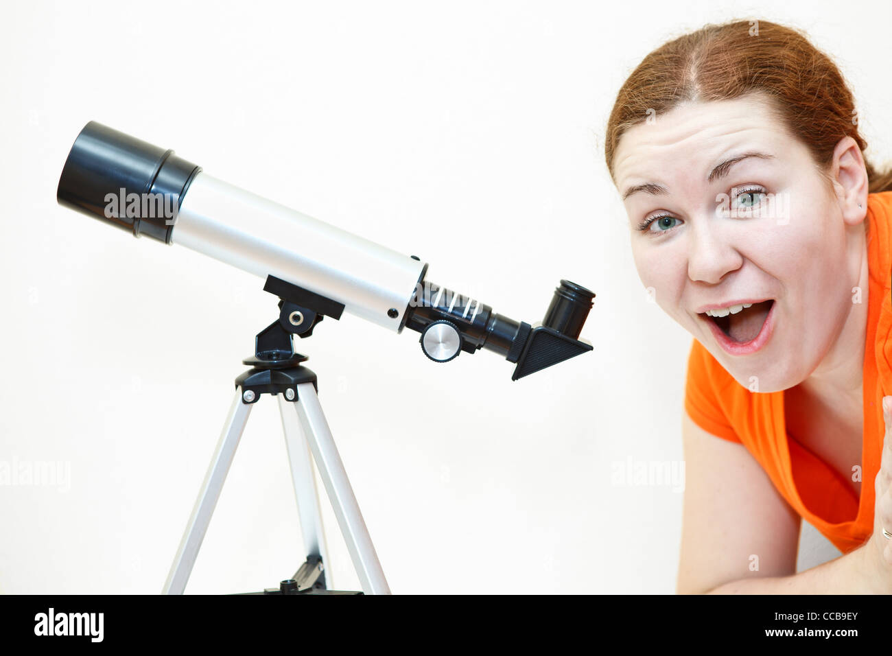 Surprised young woman in orange t-short with telescope on white background Stock Photo