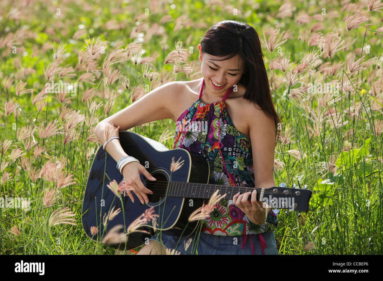 Woman playing guitar outside in grassy field. Stock Photo