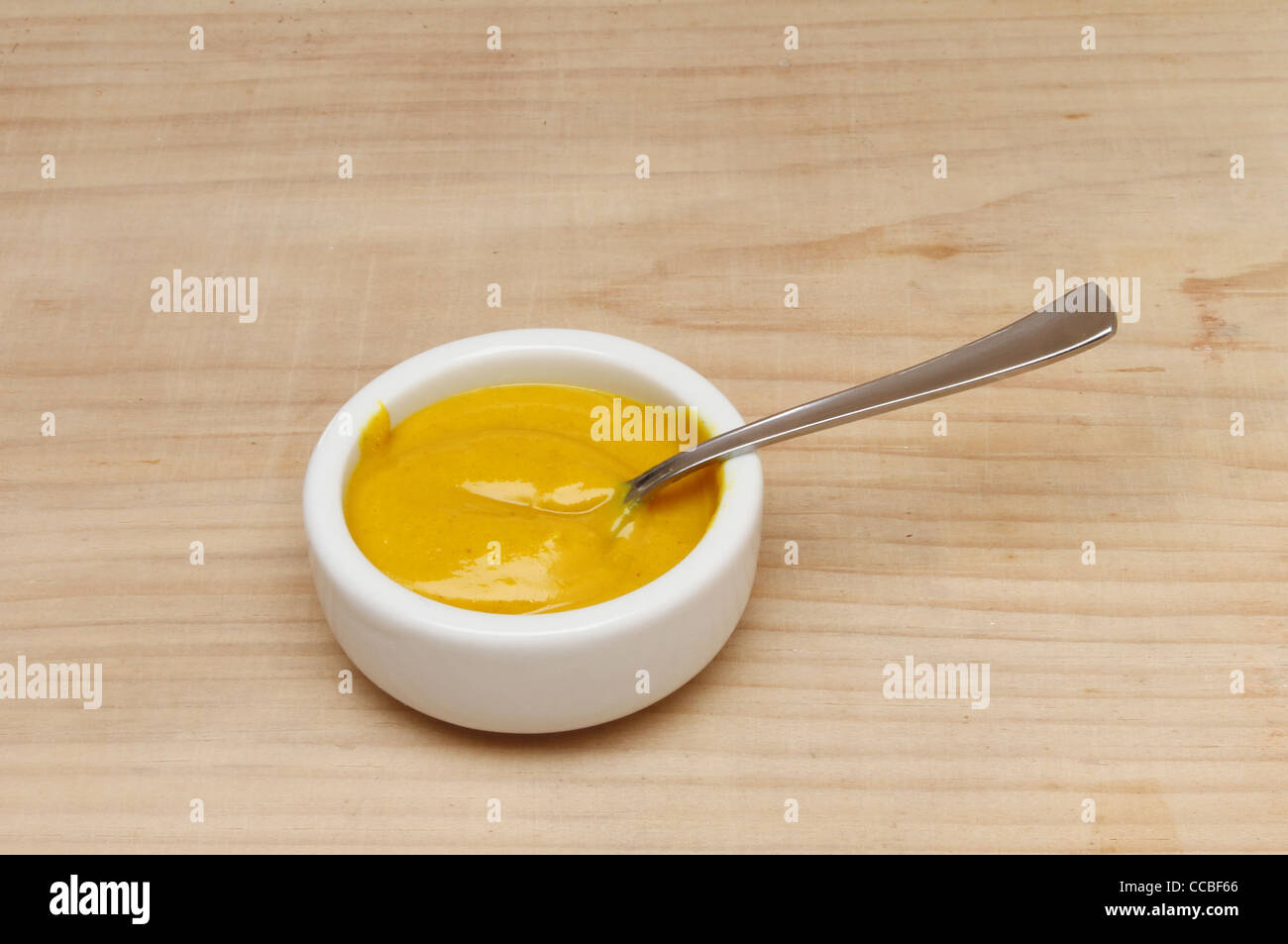 English mustard in a ramekin with a spoon on a wooden table Stock Photo