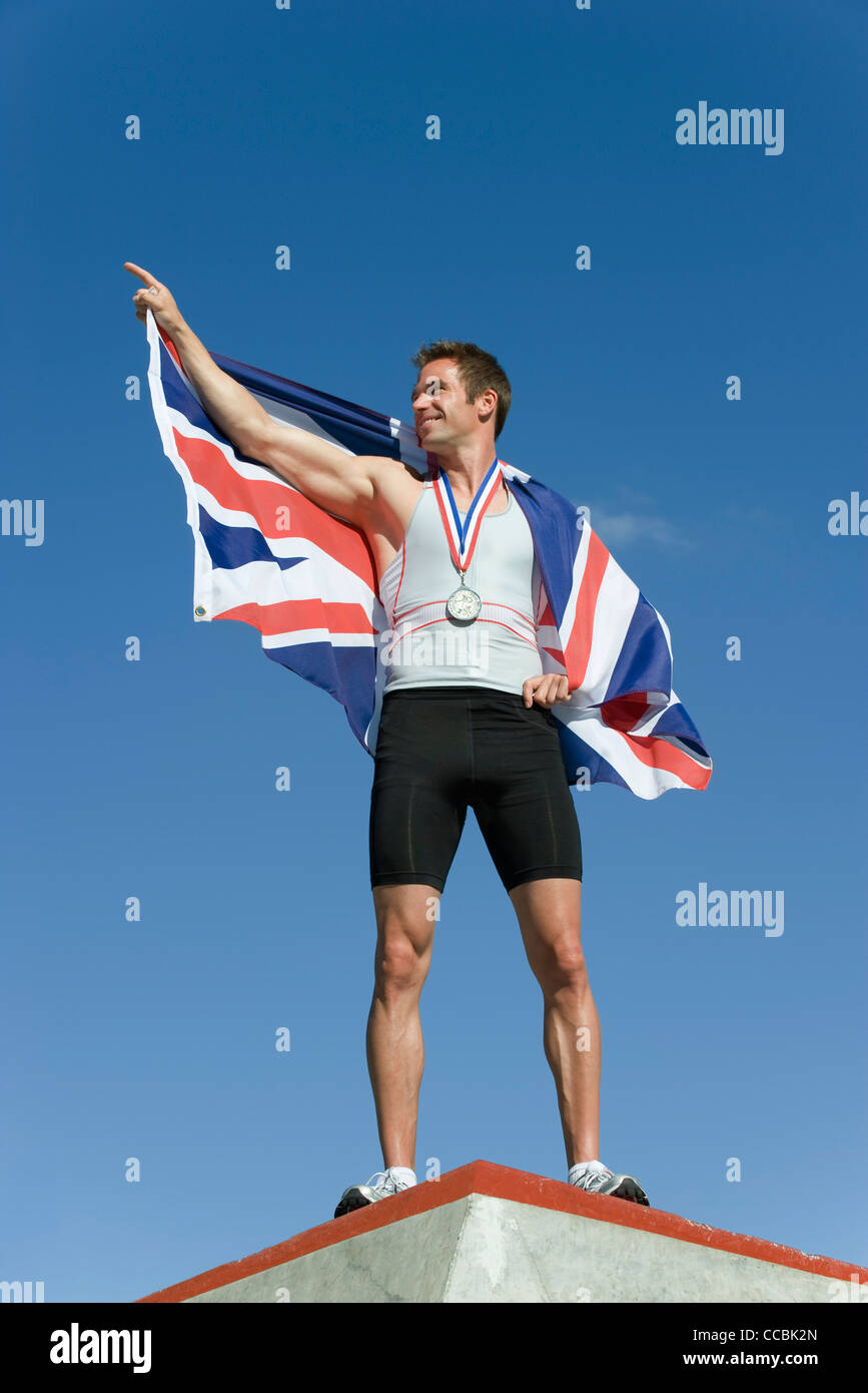 Male athlete on winner's podium, holding up British flag Stock Photo