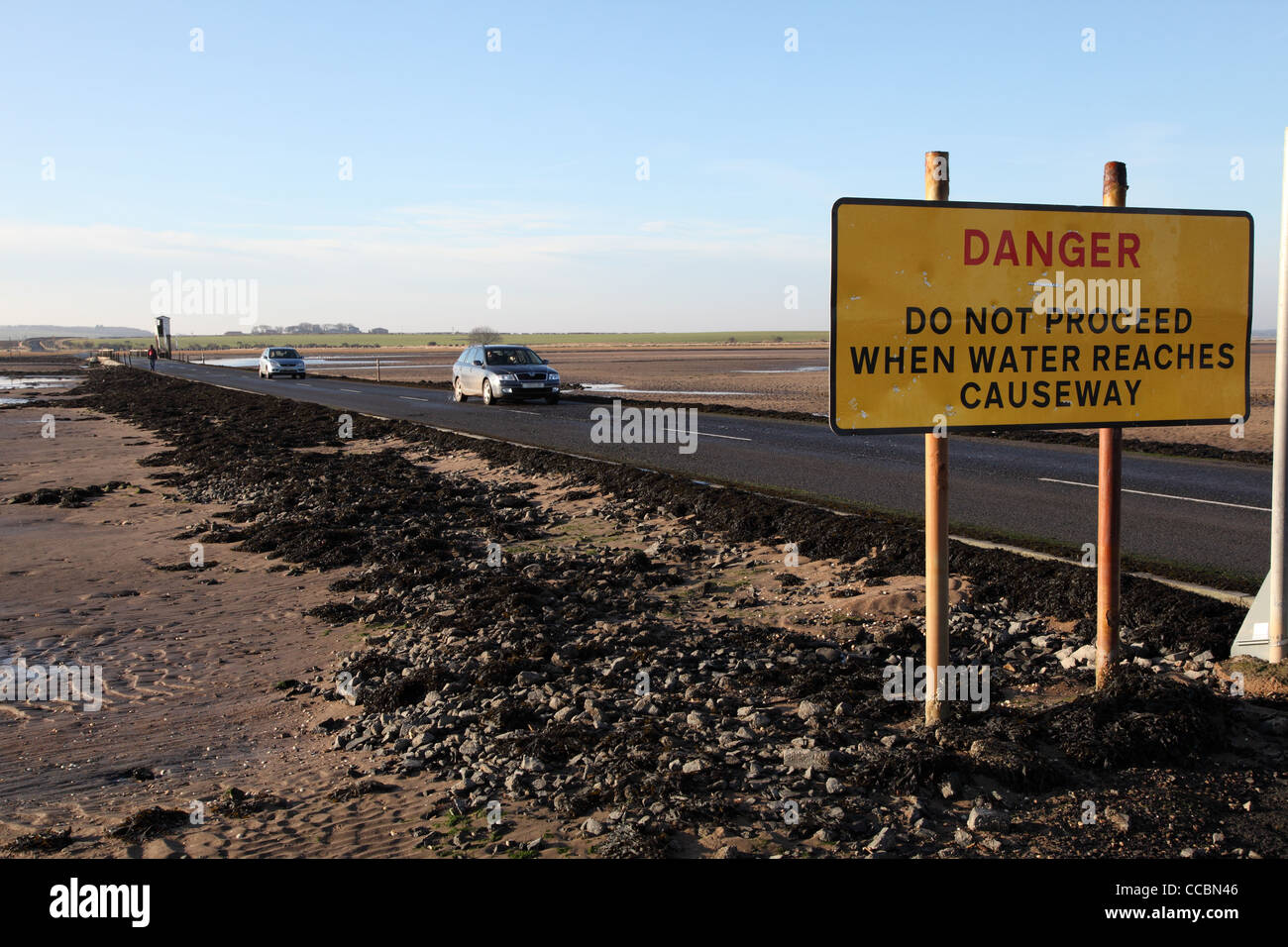 Danger notice and cars crossing the causeway at St Mary's Island, north east England UK Stock Photo