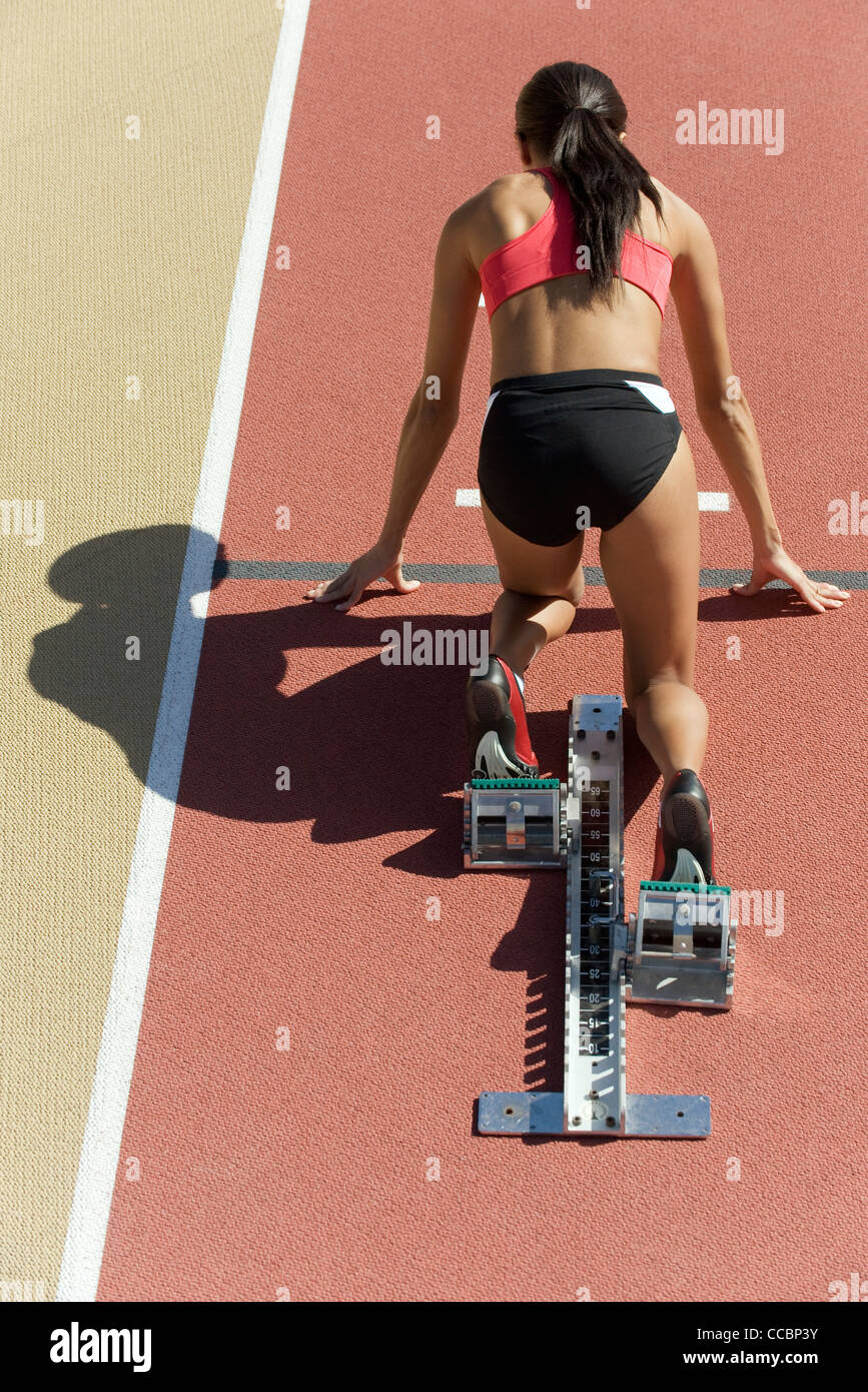 Woman crouched in starting position on running track, rear view Stock