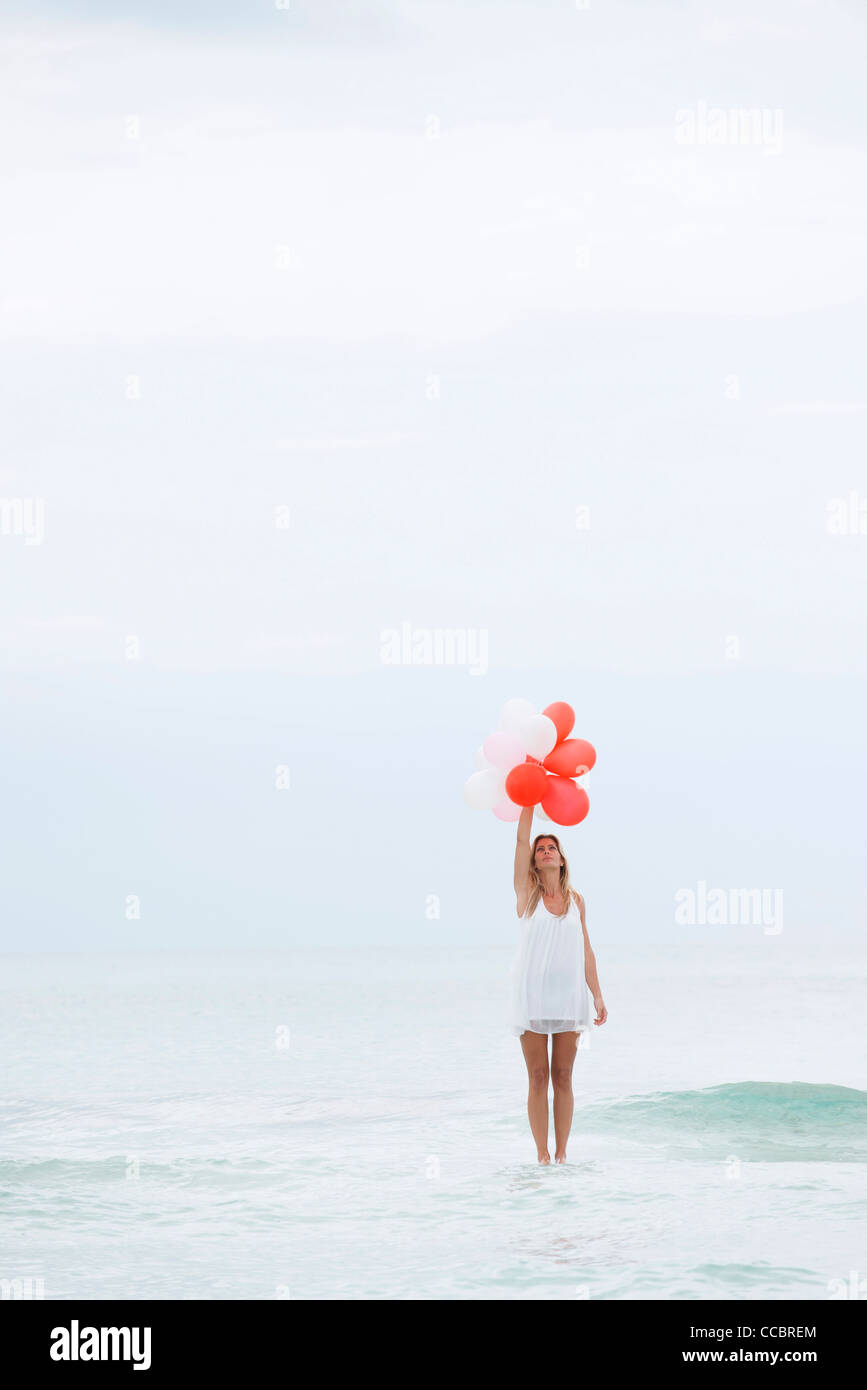 Woman standing on surface of water, holding bunch of balloons Stock Photo