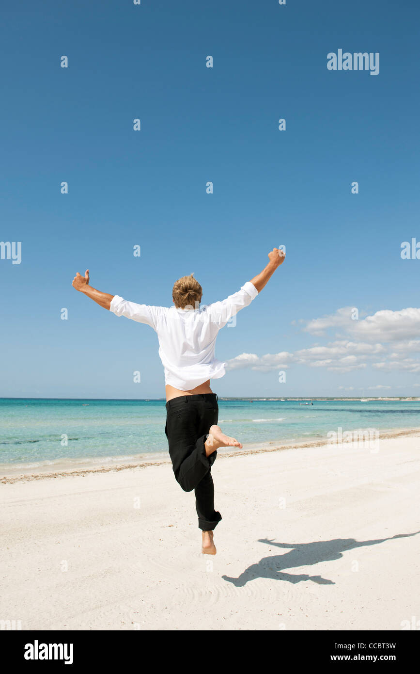 Man jumping midair on beach, rear view Stock Photo