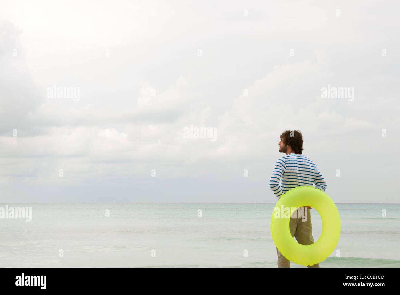 Young man with inflatable ring, looking at ocean view Stock Photo