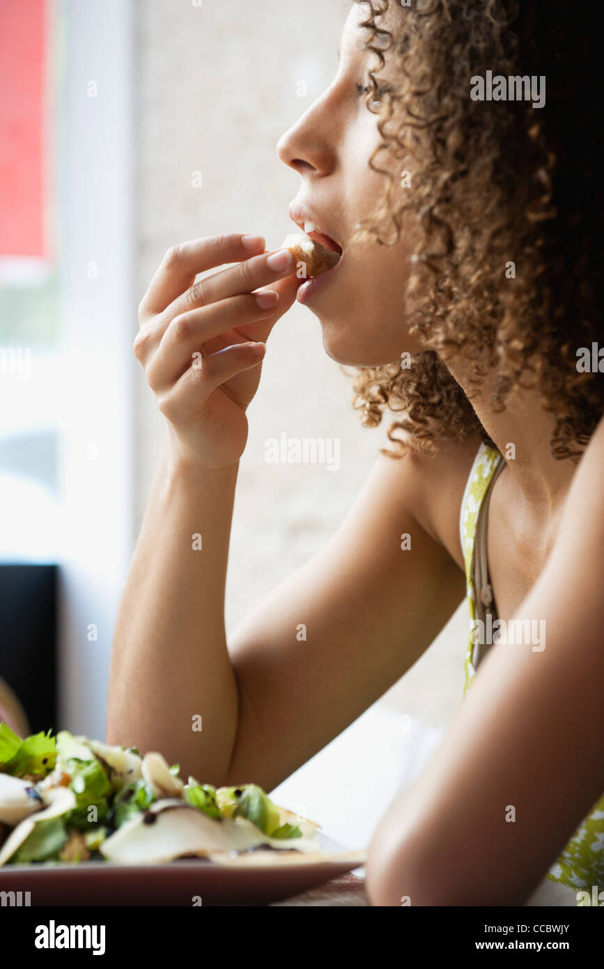 Young woman with curly hair eating salad, side view Stock Photo