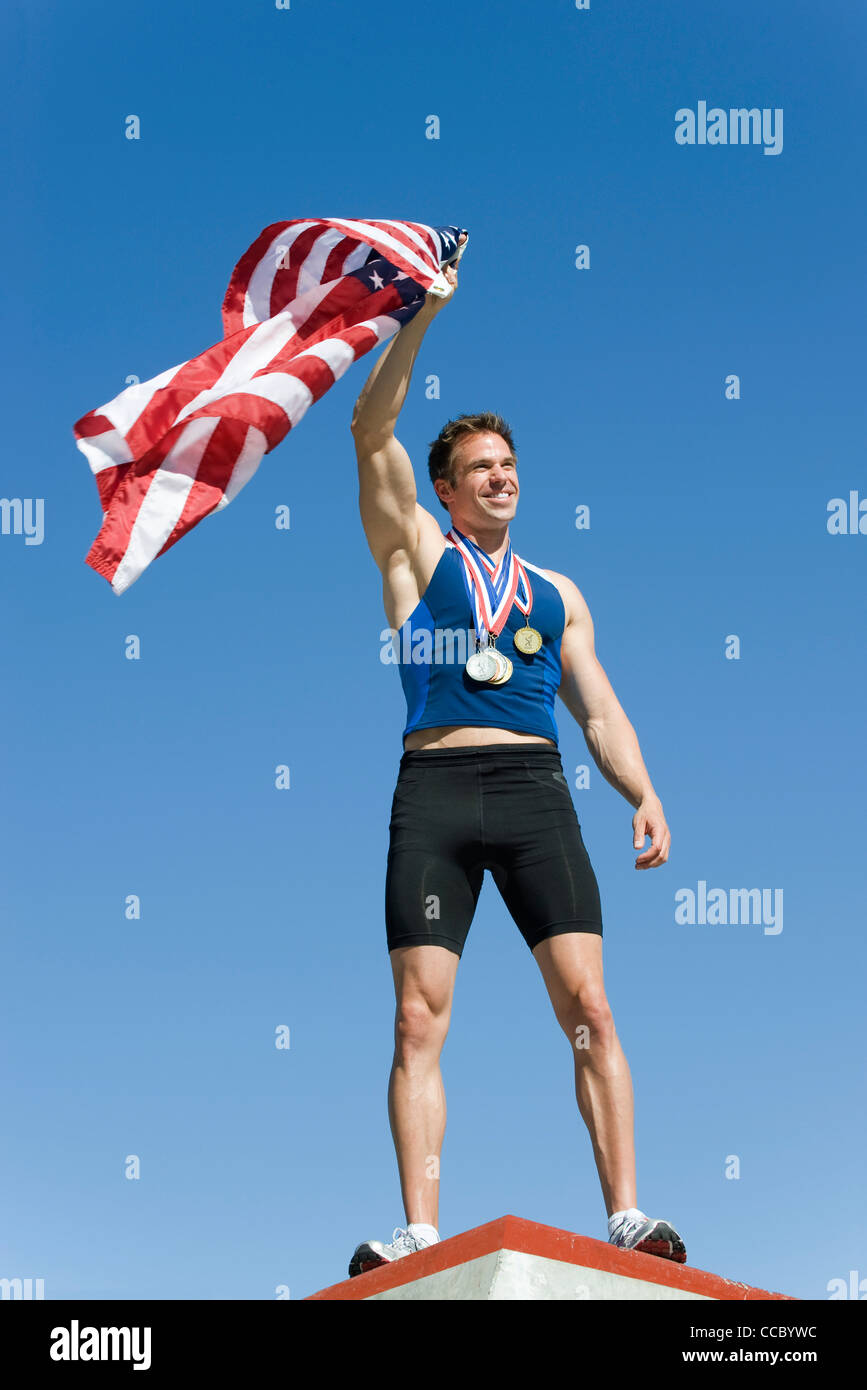 Male athlete on winner's podium, holding up American flag Stock Photo