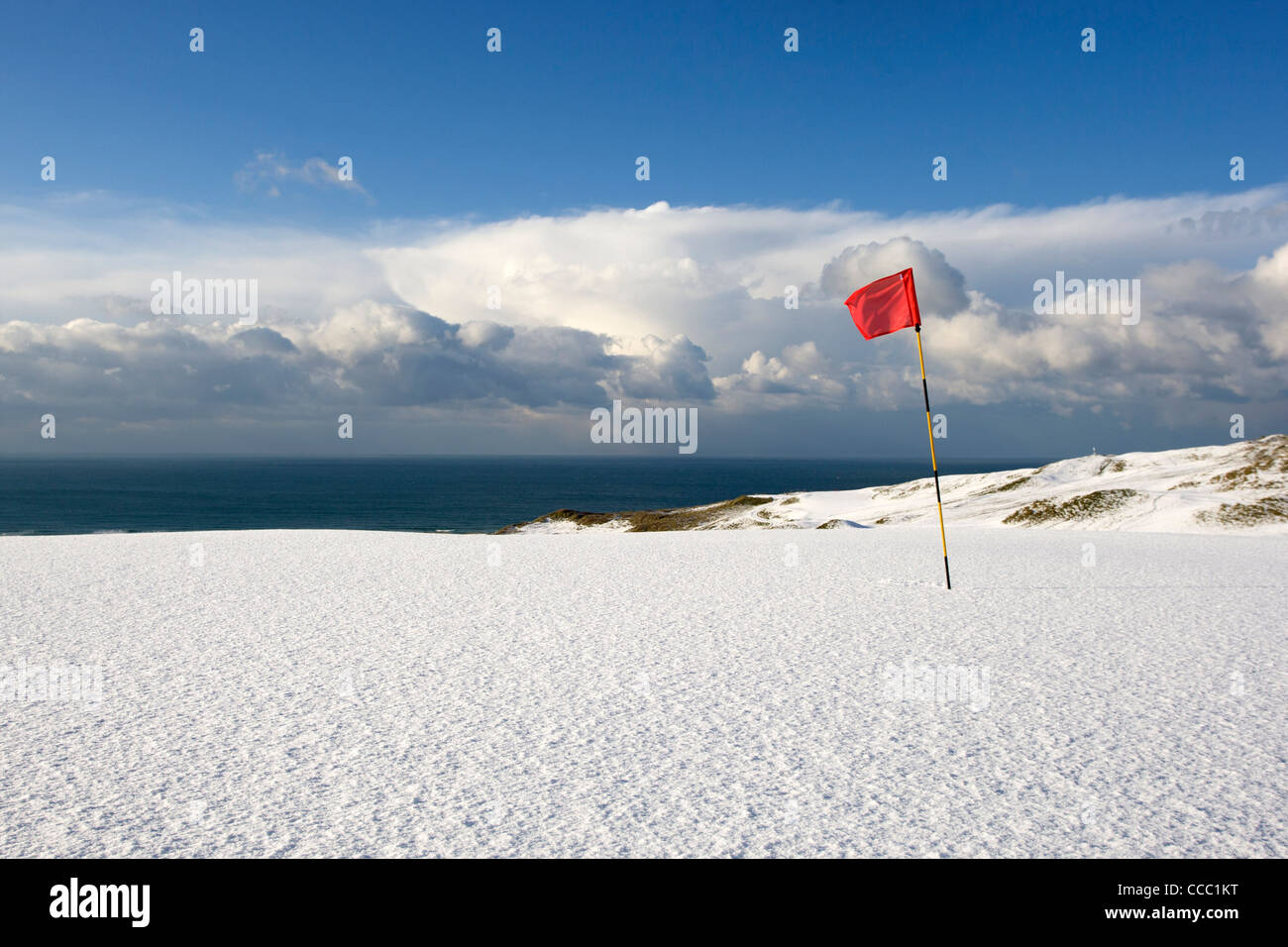 A red flag stands in the snow on one of the greens at the golf course at Perranporth Cornwall. Stock Photo