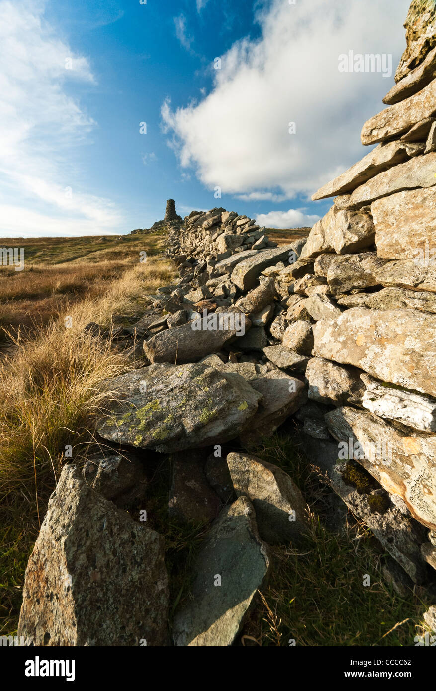 Summit of  'High Street' in the Cumbrian hills with view of a very large cairn at the end of a damaged drystone wall. Stock Photo