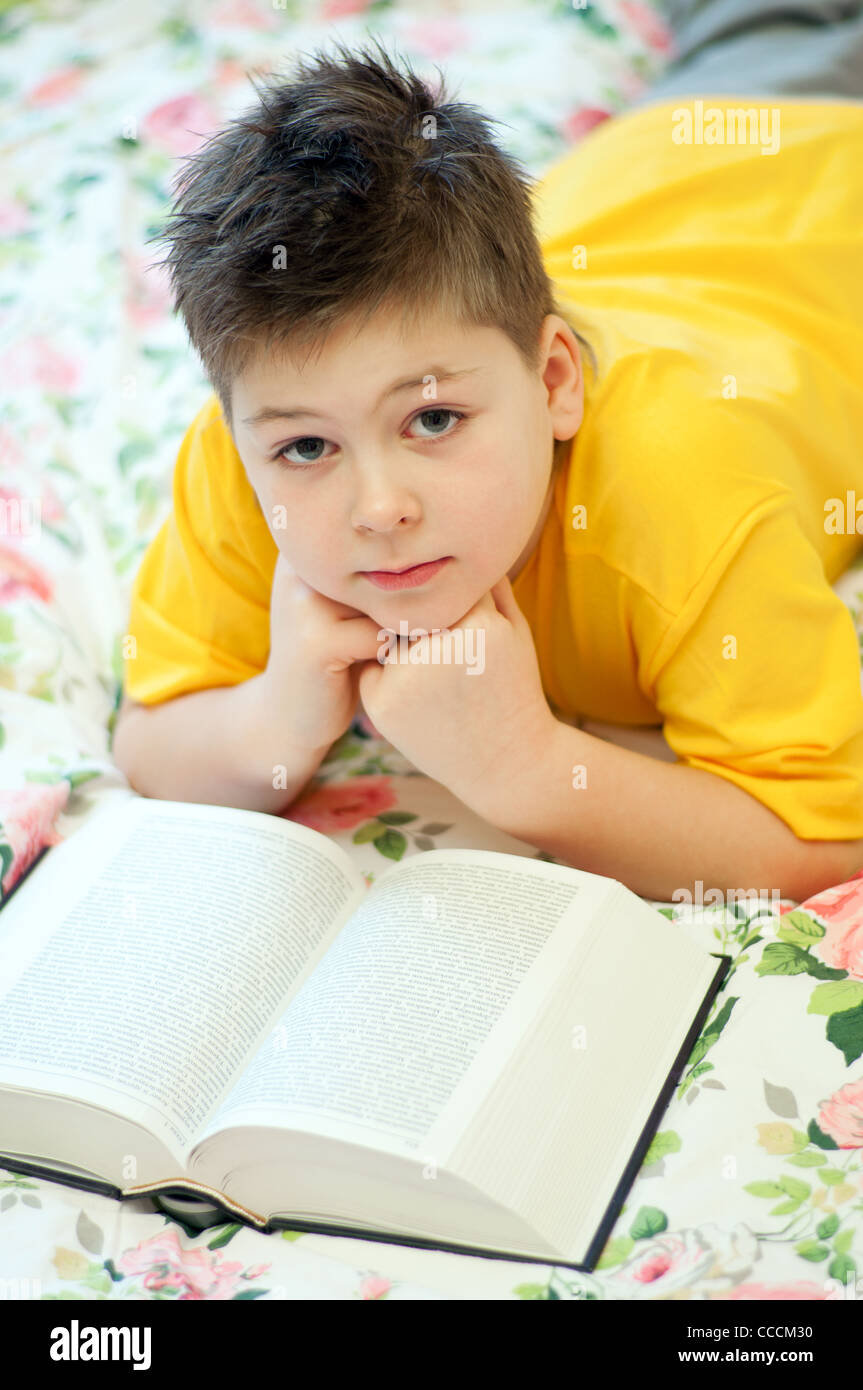 boy child 8 9 7 years reads reading learning education book printing lies lying bed bedroom blanket color flowers flower caucasi Stock Photo