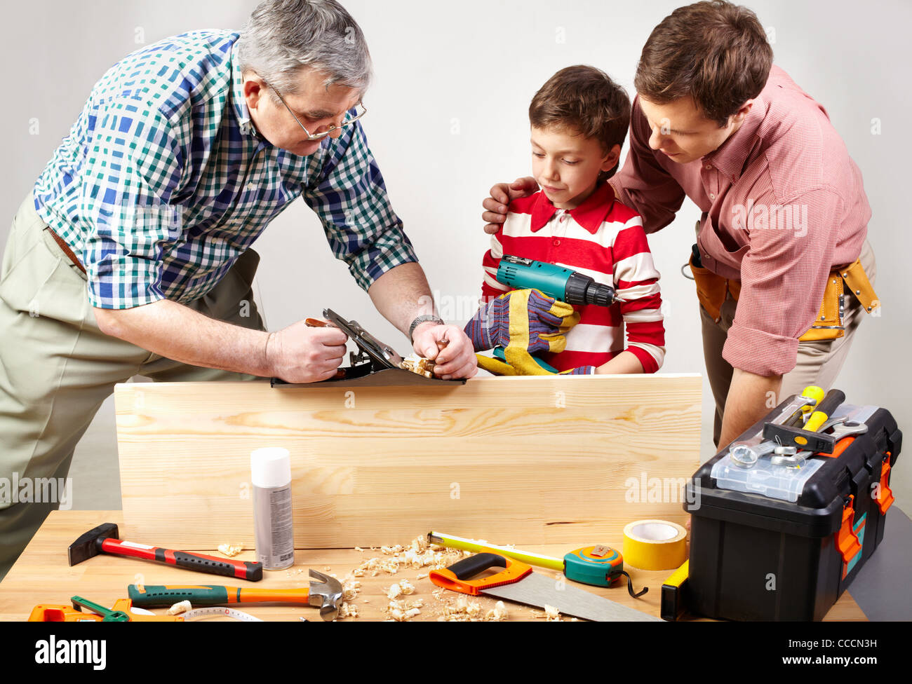 A grandfather and a father teaching a boy to work with plane Stock Photo