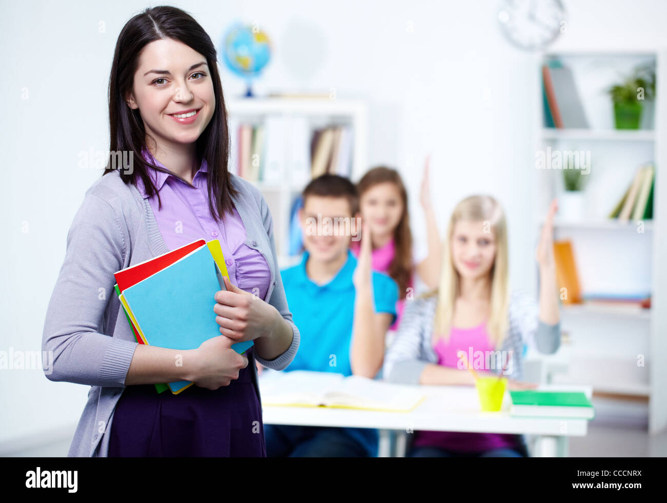 Happy teacher looking at camera with her students on background Stock ...