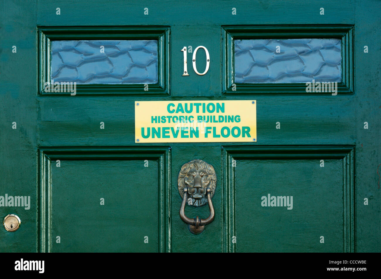 Sign on a green door warns of uneven floors in an old building. Stock Photo