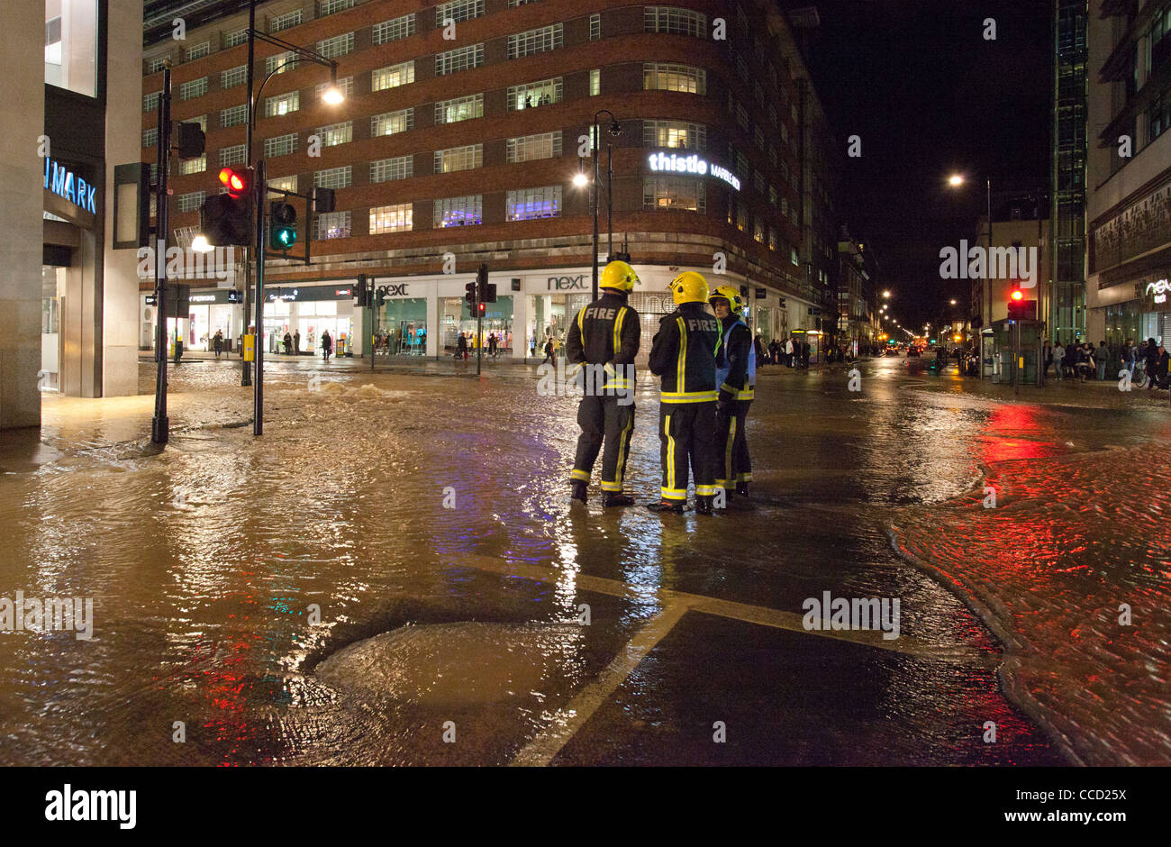 Firemen standing in floodwater on Oxford Street after mains water pipe