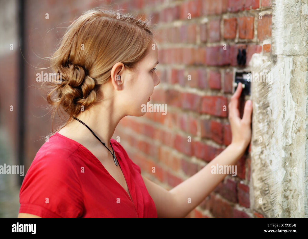 Pretty young blond woman rings at the door bell Stock Photo