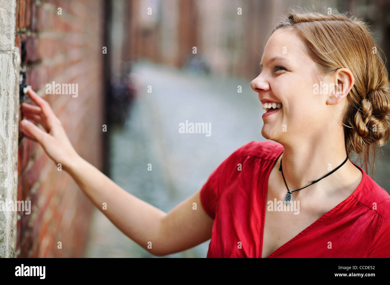 Pretty young smiling woman ringing at the door bell Stock Photo