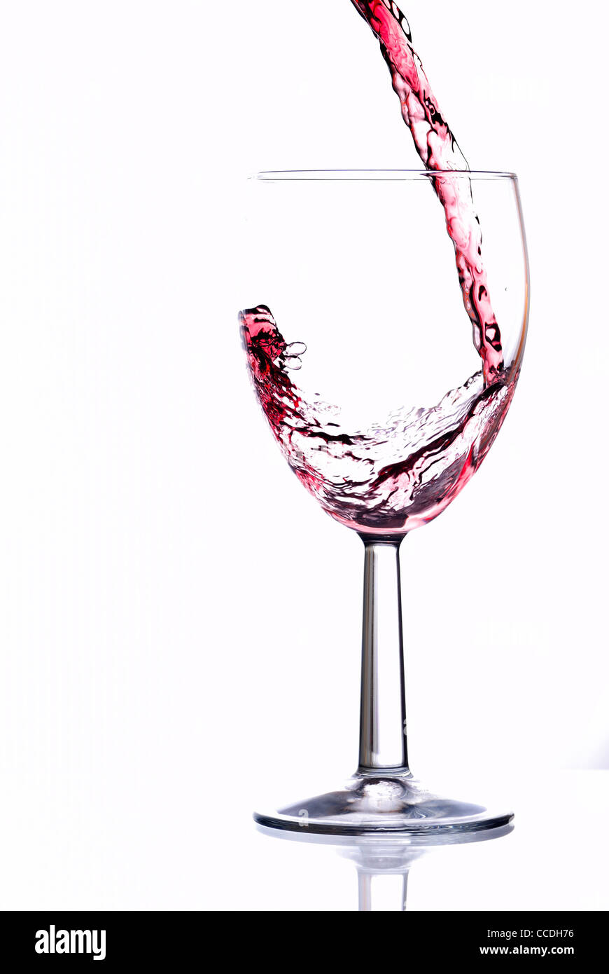 Red wine pouring into wine glass. White background, reflexion Stock