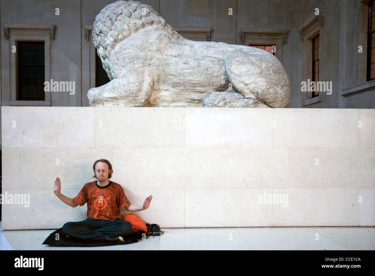 A man performs qi gong exercises - part of a meditation flash mob in the Great Court of the British Museum beneath a lion statue Stock Photo