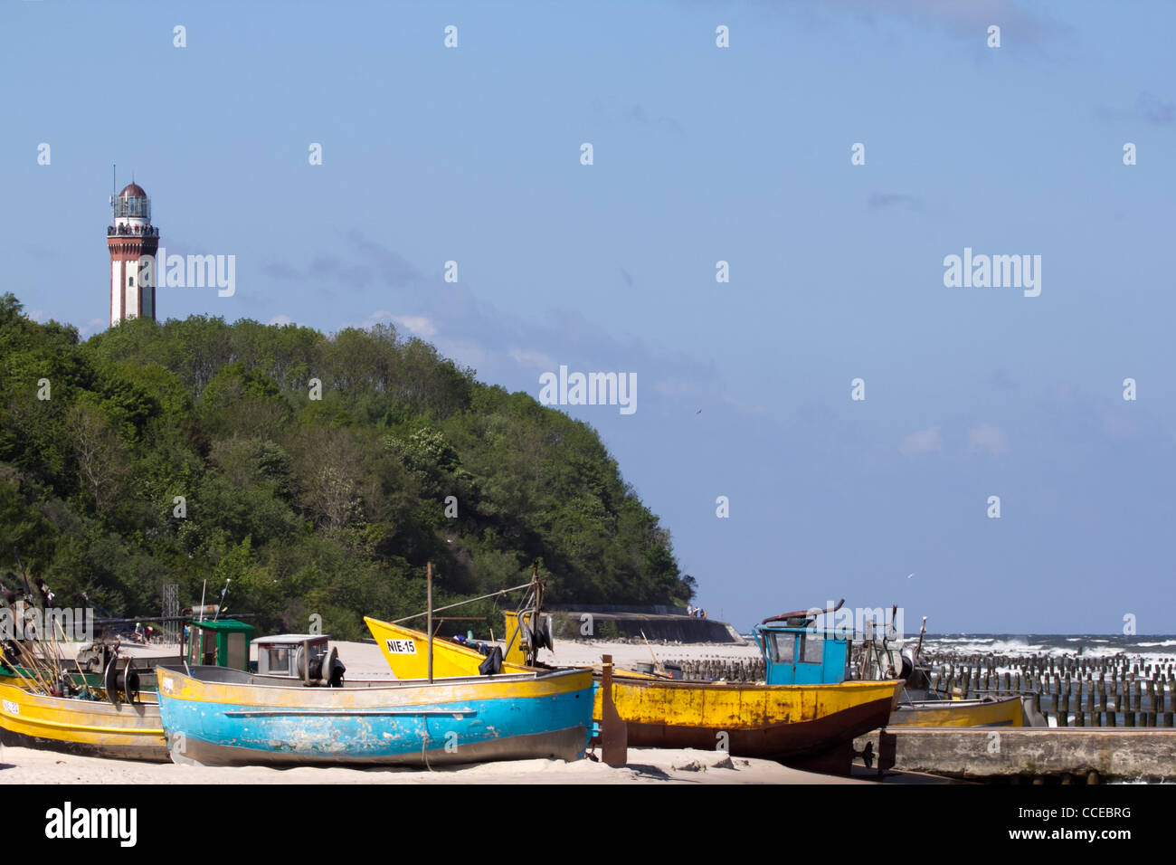 Fishing Boats on the beach in Niechorze. In the background, surrounded by trees you can see the lighthouse. Stock Photo