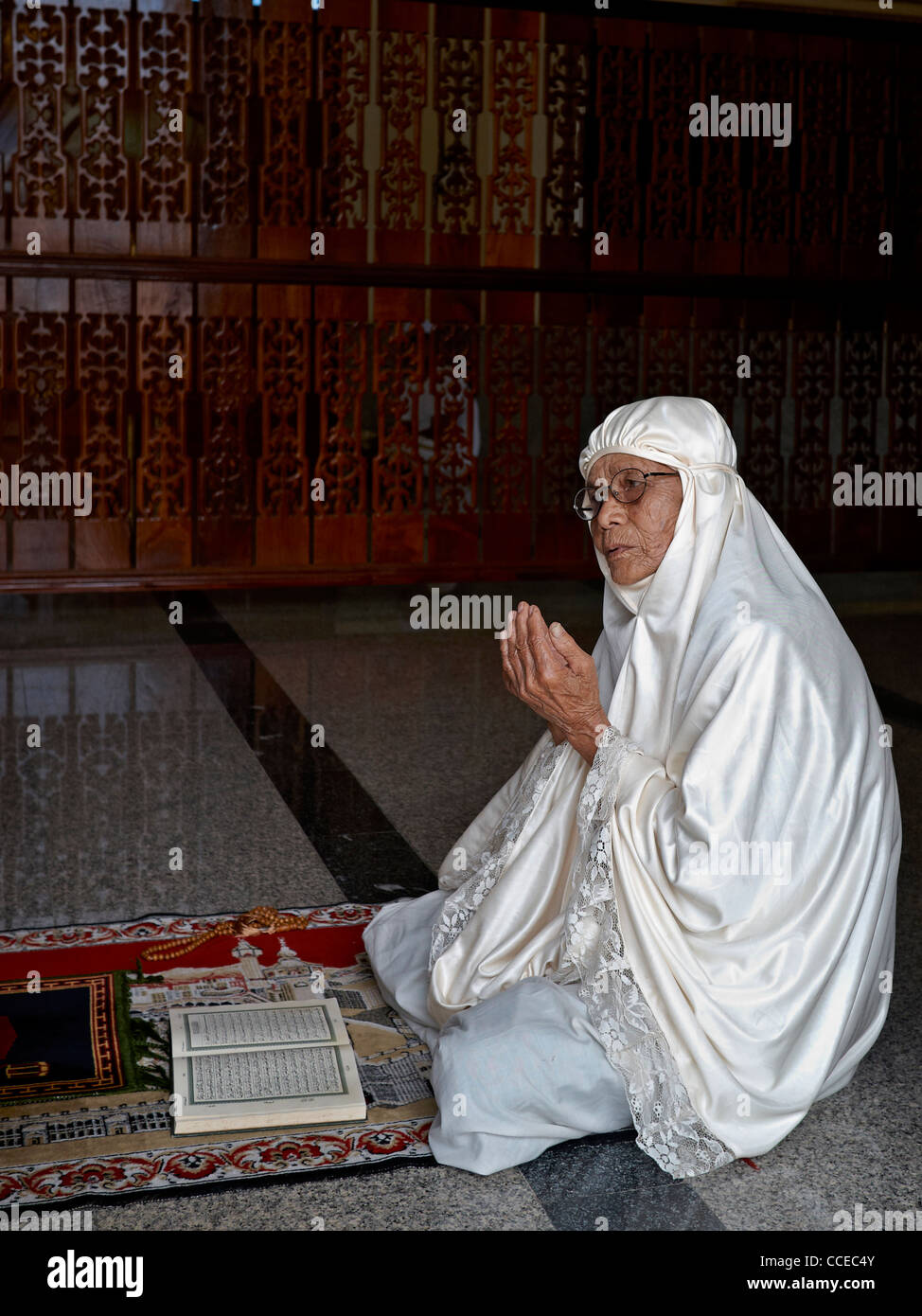 90 year old Muslim woman praying and wearing a white traditional burka Stock Photo