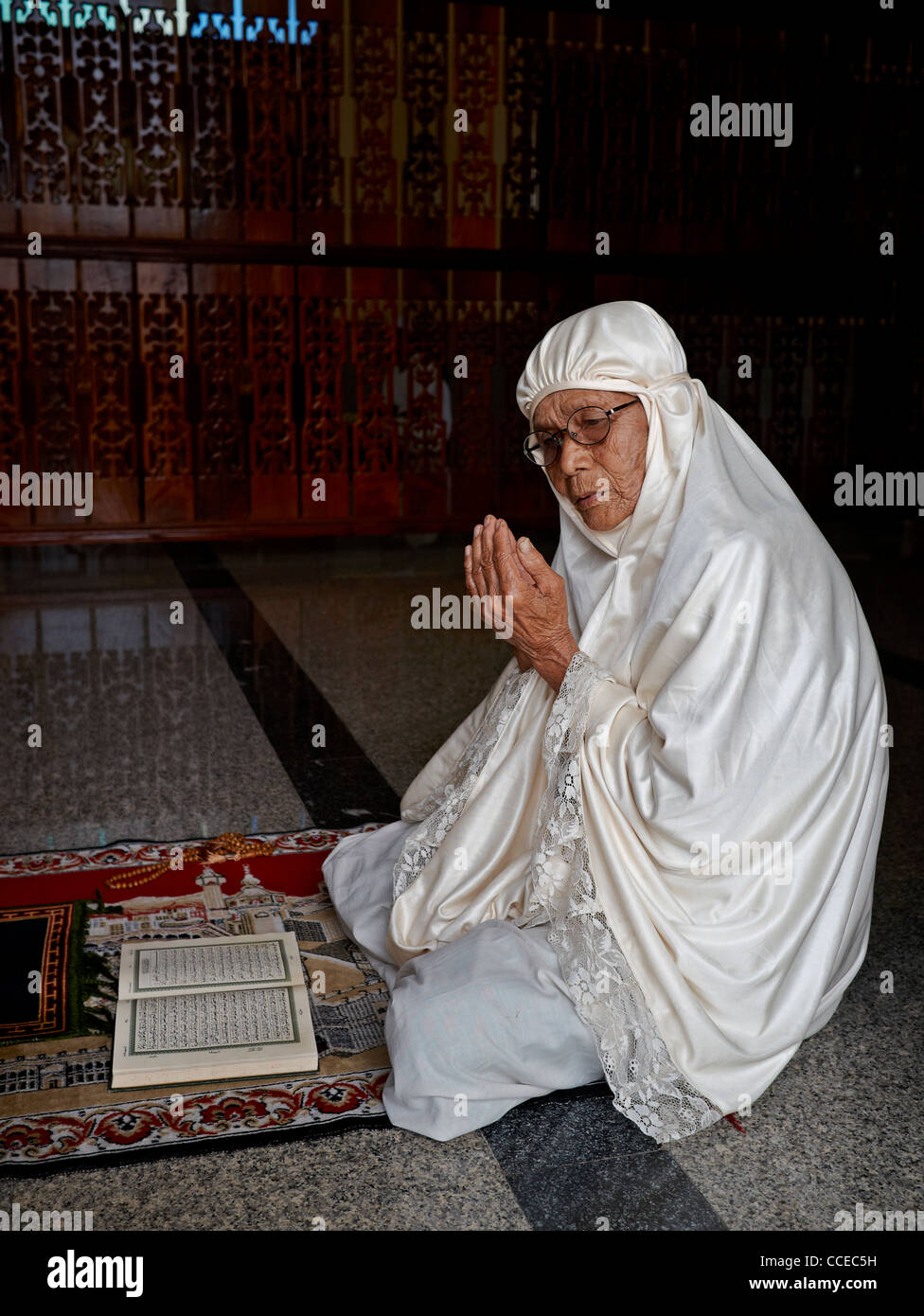 90 year old Muslim woman praying and wearing a white traditional burka Stock Photo