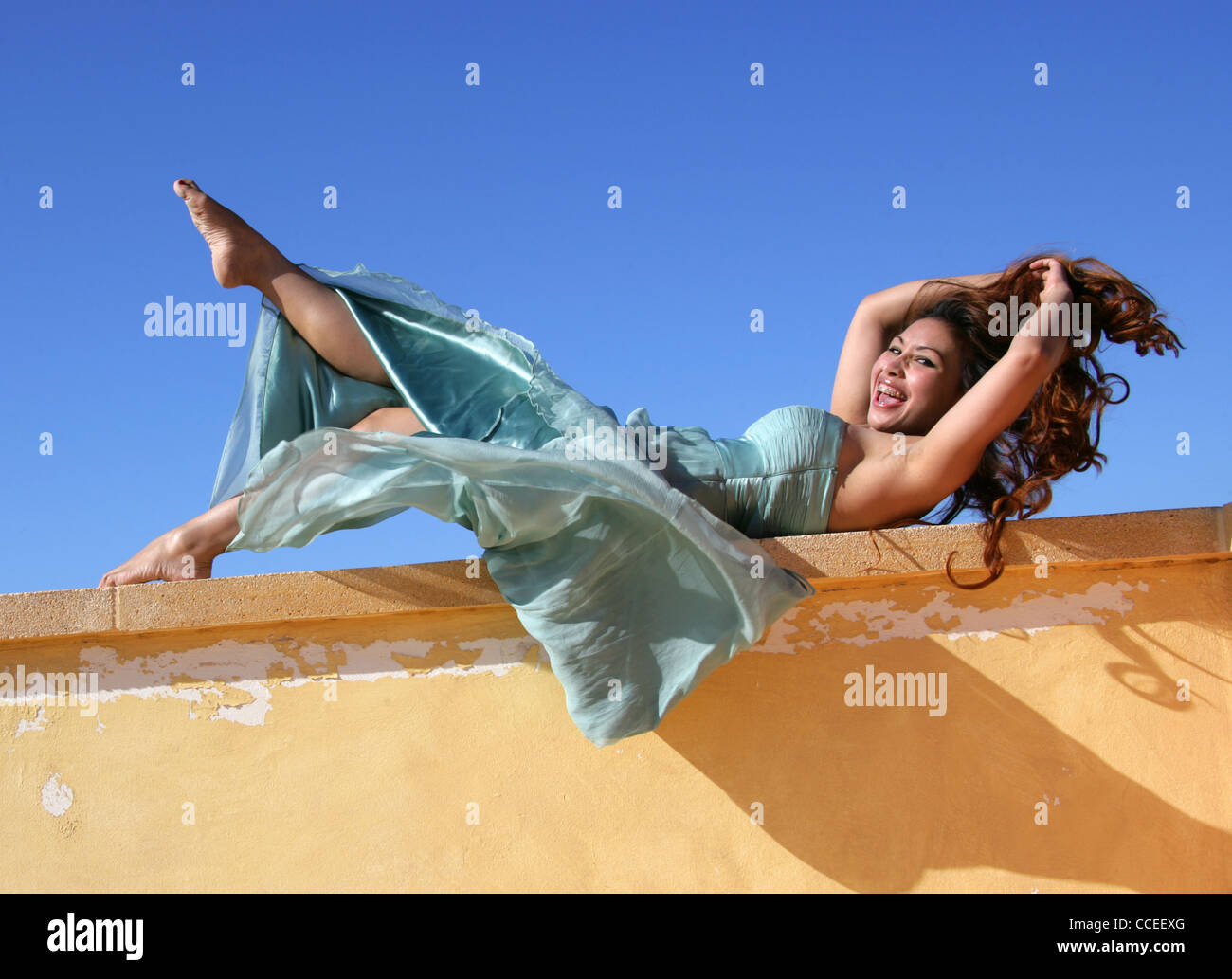 Indonesian Girl in a Turquoise Dress Laying on a Yellow Wall, Fuerteventura, Canary Islands, Spain. Stock Photo