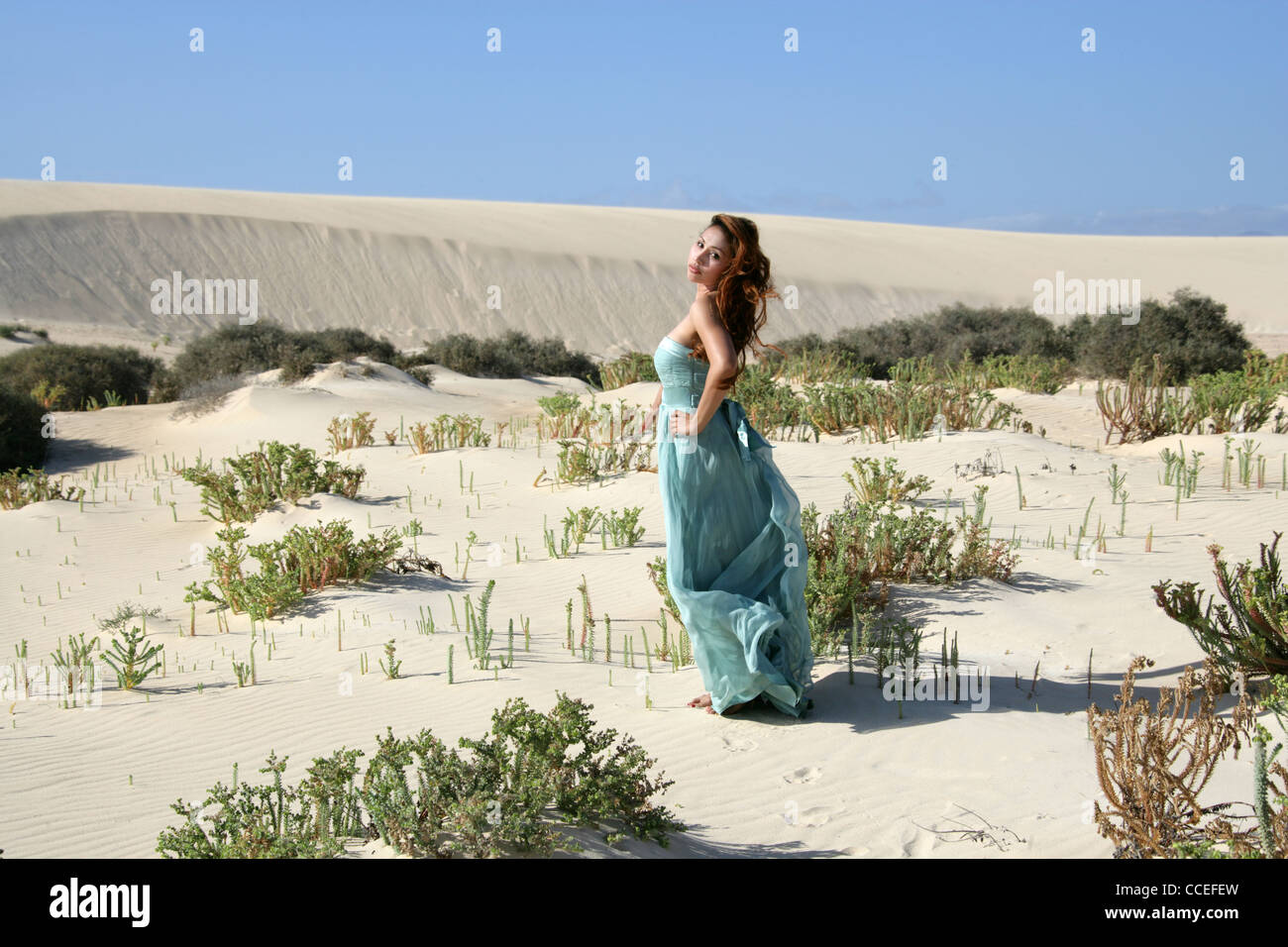 Indonesian Girl in a Turquoise Dress Running on Sand Dunes, Fuerteventura, Canary Islands, Spain. Stock Photo