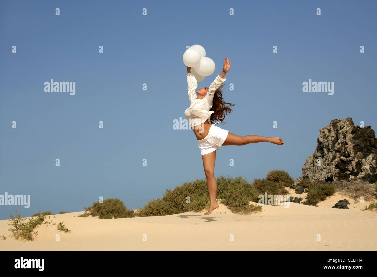 Indonesian Girl in a White Outfit with Balloons Jumping on Sand Dunes,  Fuerteventura, Canary Islands. Stock Photo