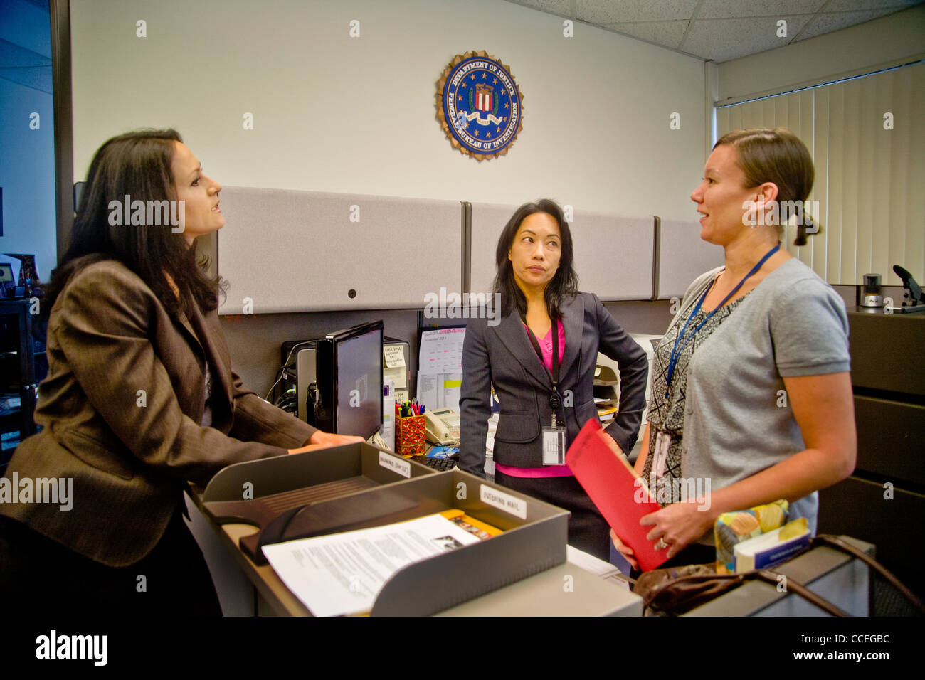 Three female FBI agents discuss a case in Santa Ana, CA, office. Note Filipino-American in center and FBI logo on wall. RELEASED Stock Photo