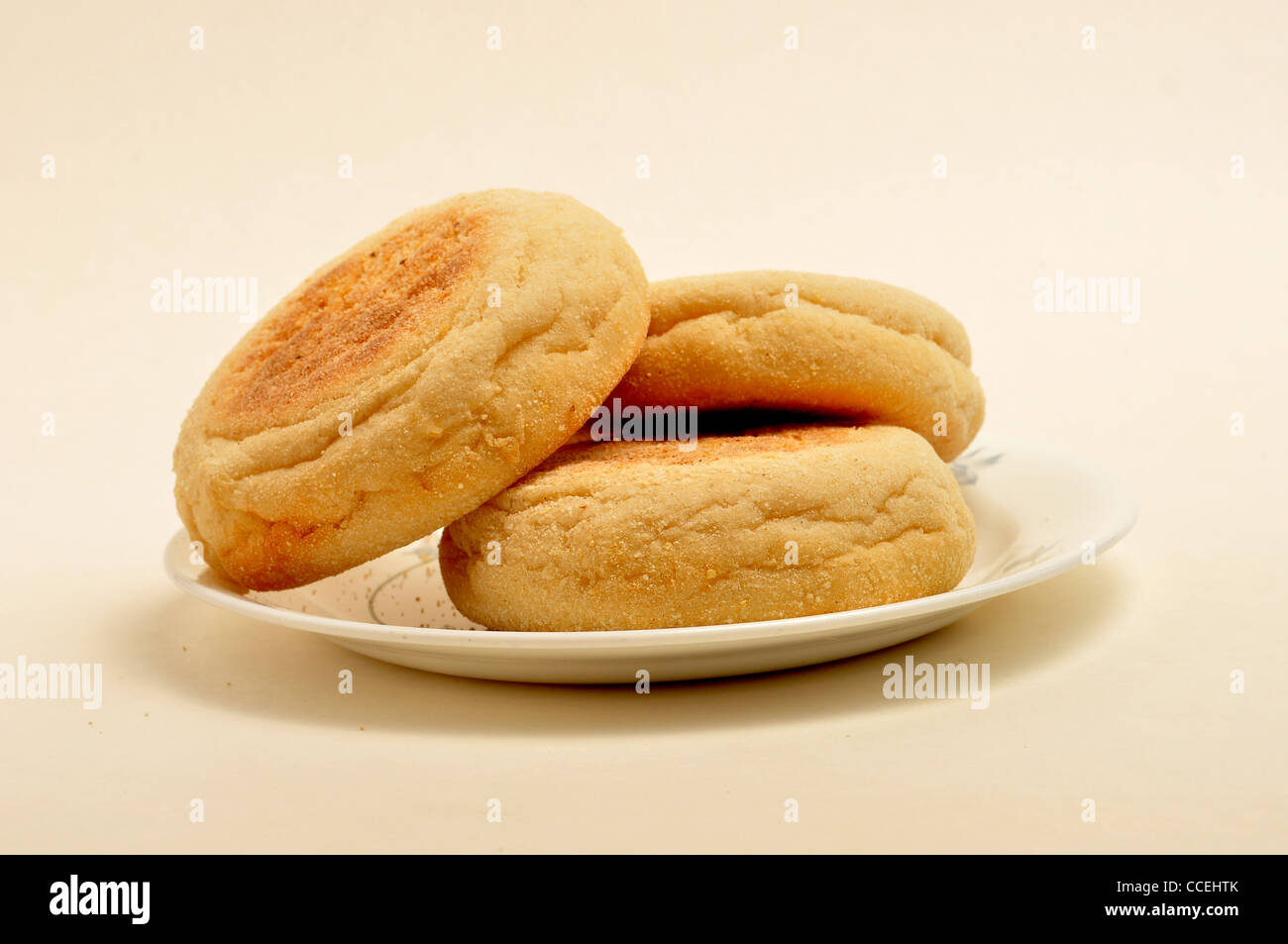 3 English muffins sit on a small saucer on a plain background. Stock Photo