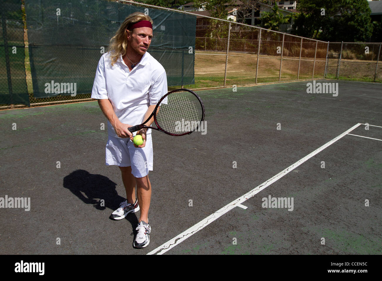 A blonde male tennis player gets prepared to make a strong overhand serve over the net. Stock Photo