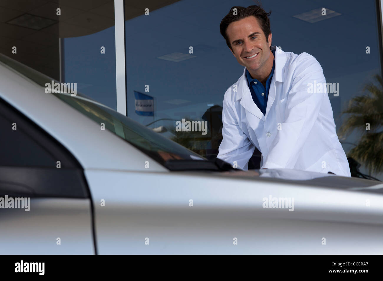 Cheerful car dealer standing besides car Stock Photo