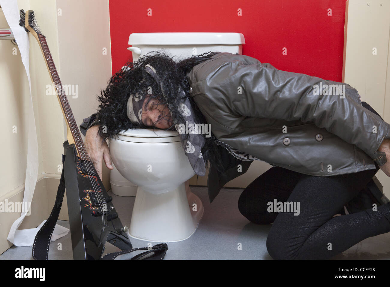 Exhausted senior male guitarist sleeping in toilet Stock Photo