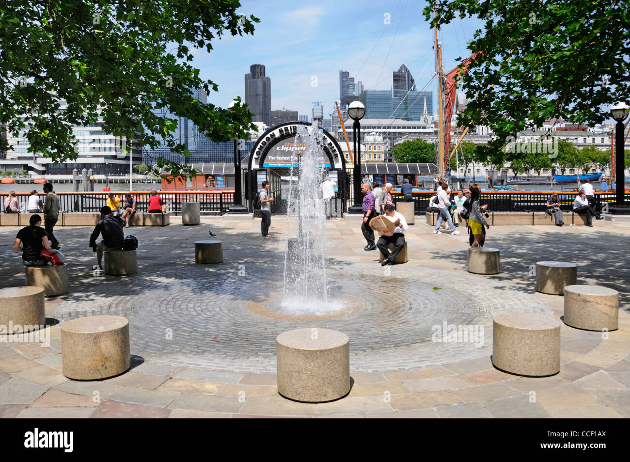 Fountain water feature & paved area outside entrance to London Bridge City pier beside the River Thames with city skyline beyond Southwark London UK Stock Photo