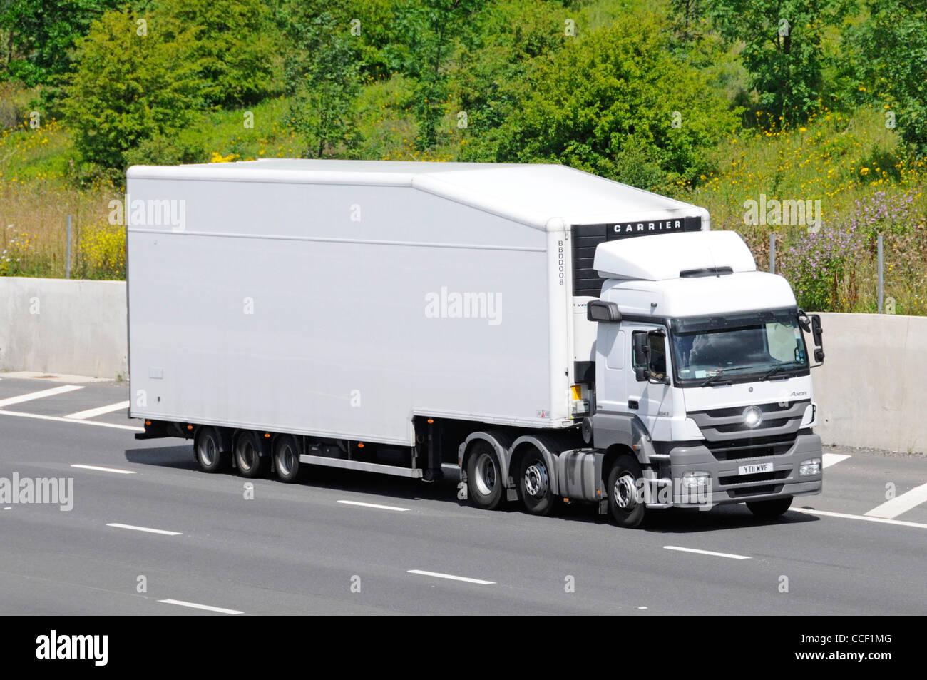 Side and front of white unmarked clean hgv delivery lorry truck and articulated aerodynamic shape trailer driving along M25 motorway Essex England UK Stock Photo