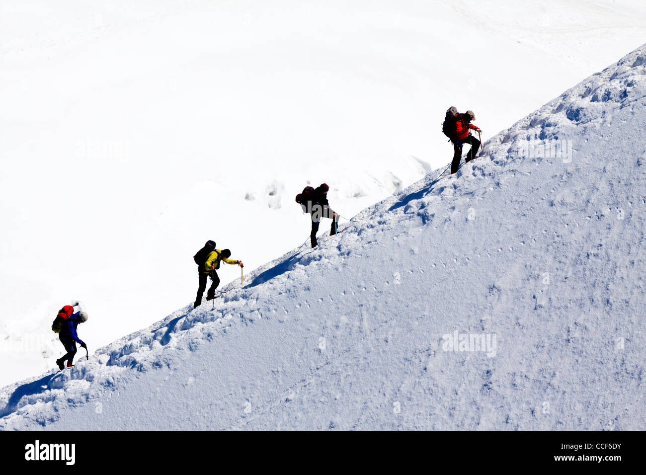 Mountain climbers ascending ice covered ridge in snow near summit of
