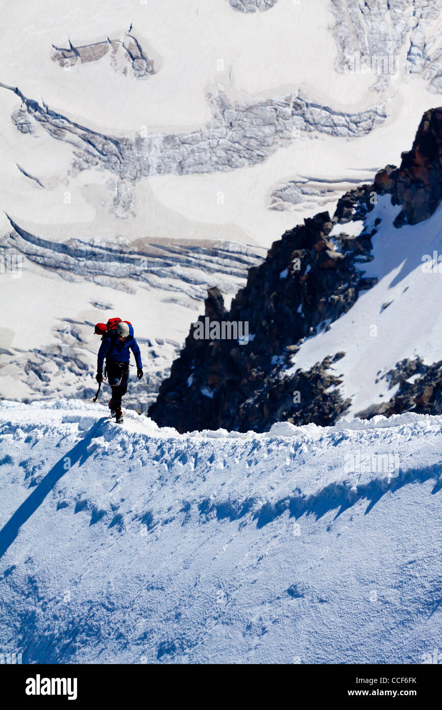 Mountain climber ascending ice covered ridge in snow near summit of ...