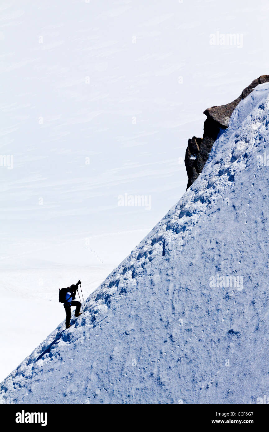 Mountain climber ascending ice covered ridge in snow near summit of ...