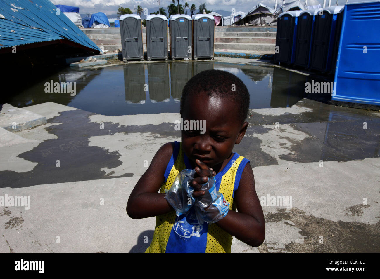 Nov 10, 2010 - Port-au-Prince, Haiti.A young residents of a tent city in the Cite Soleil area of Port-au-Prince, Haiti wears water bags as gloves in an effort, his older sisiter said, to avoid getting cholera, as other residents gather water from pipes just yards from portable toilets and flood wate Stock Photo