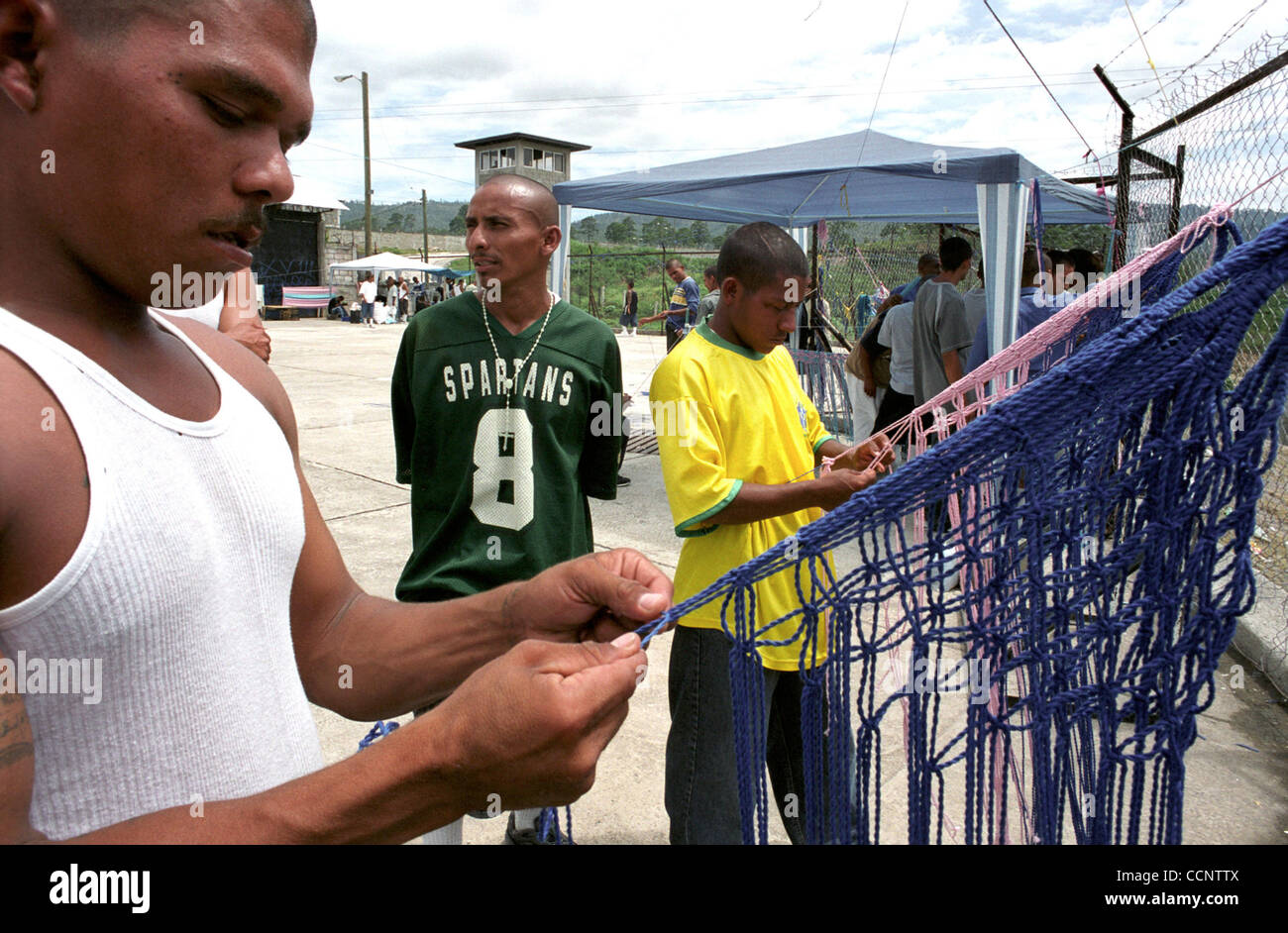 Little Cuervo,' 25, (left, foreground) and Carlos, 23, (right, background) weave yarn into fabric bags in a cellblock at a federal penitentiary near Tegucigalpa, Honduras. The 18th Street gang members earn money by giving the bags to relatives to sell outside the prison.   Photographer:  Luis J. Jim Stock Photo